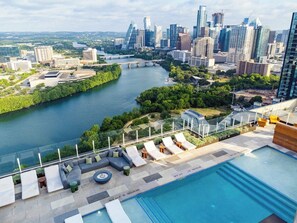 Una piscina sul tetto con lettini, sullo sfondo il profilo urbano di una città e un fiume.