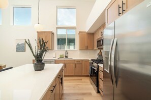 Una cocina moderna con armarios de madera, un refrigerador de acero inoxidable y una isla grande con una planta en maceta.