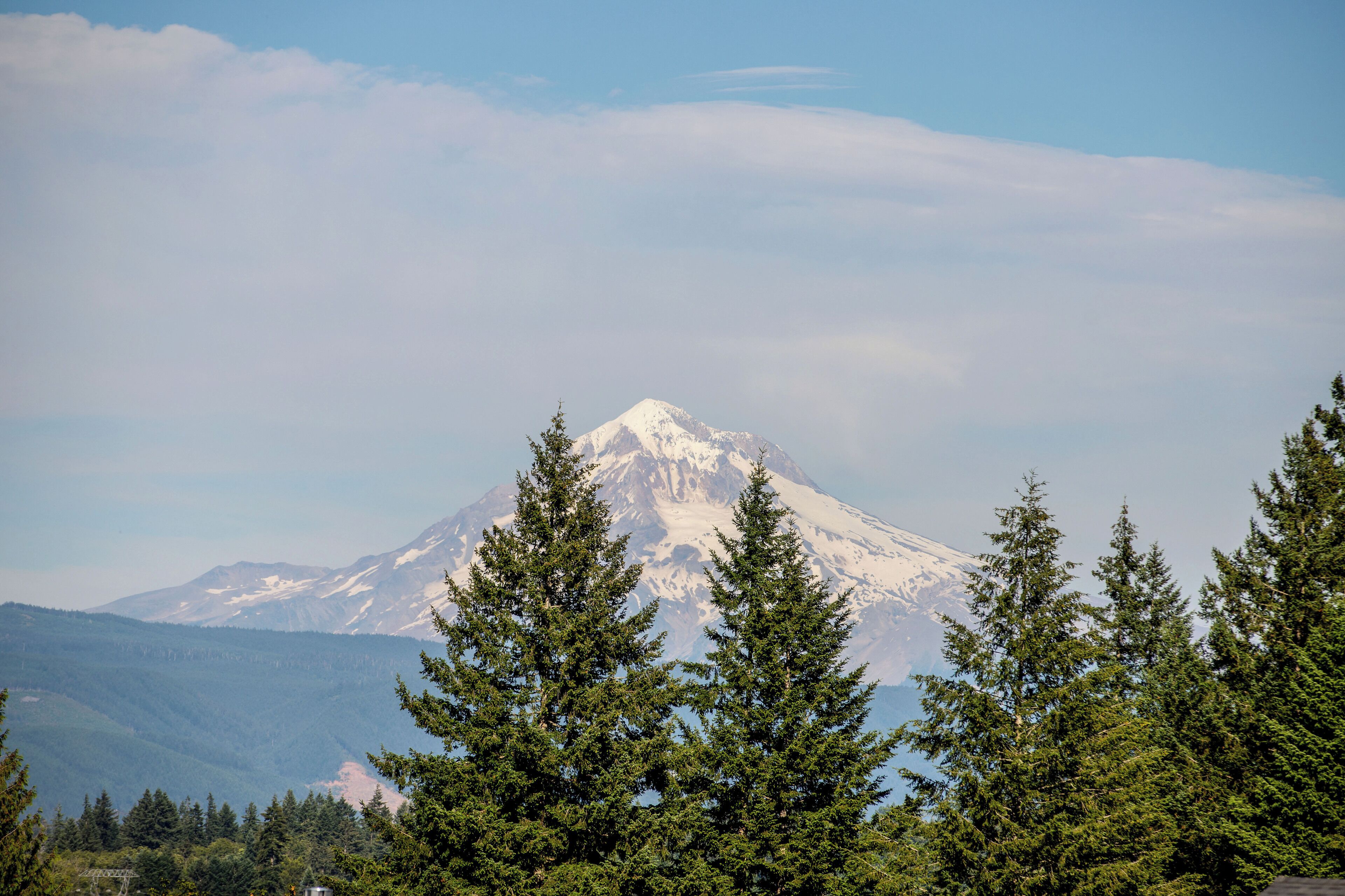 A mountain with snow-capped peaks, surrounded by evergreen trees.
