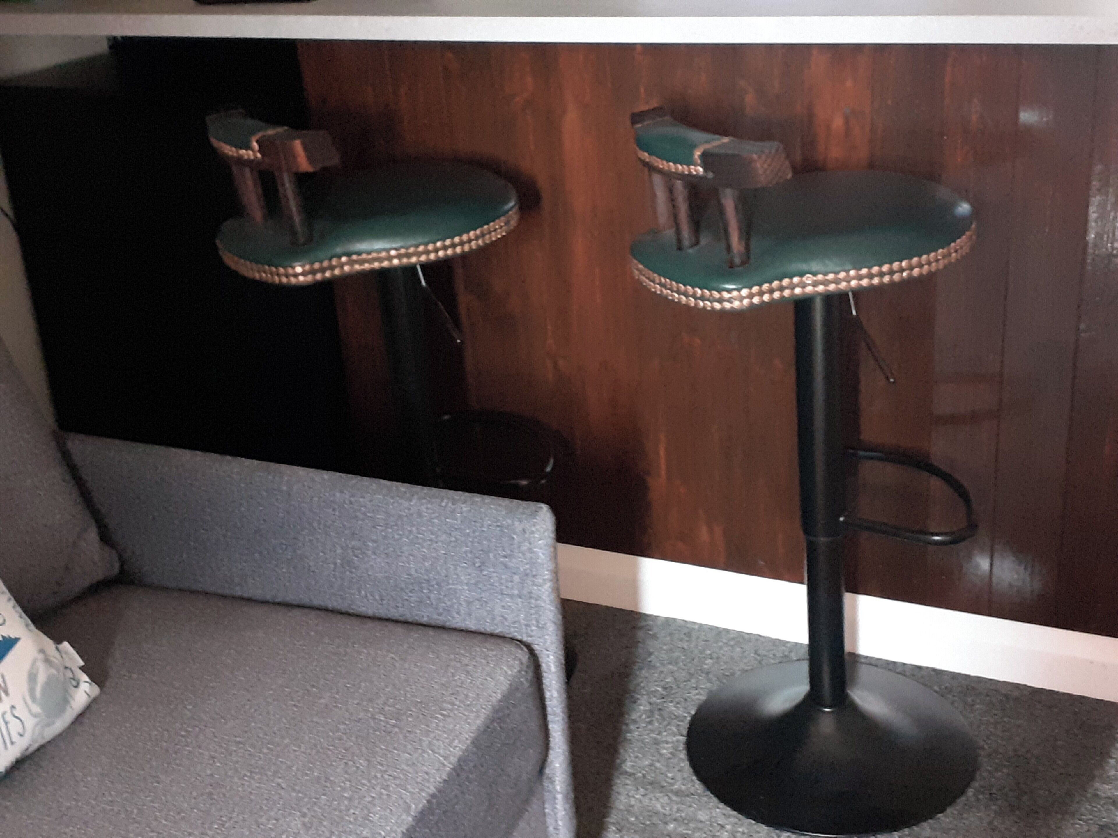 Twee barkrukken met beklede zittingen en een rond voetstuk, voor een houten wand.