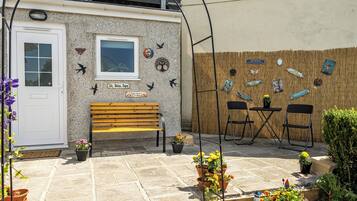 A small outdoor seating area with a bench and chairs, surrounded by potted plants and decorative wall art.
