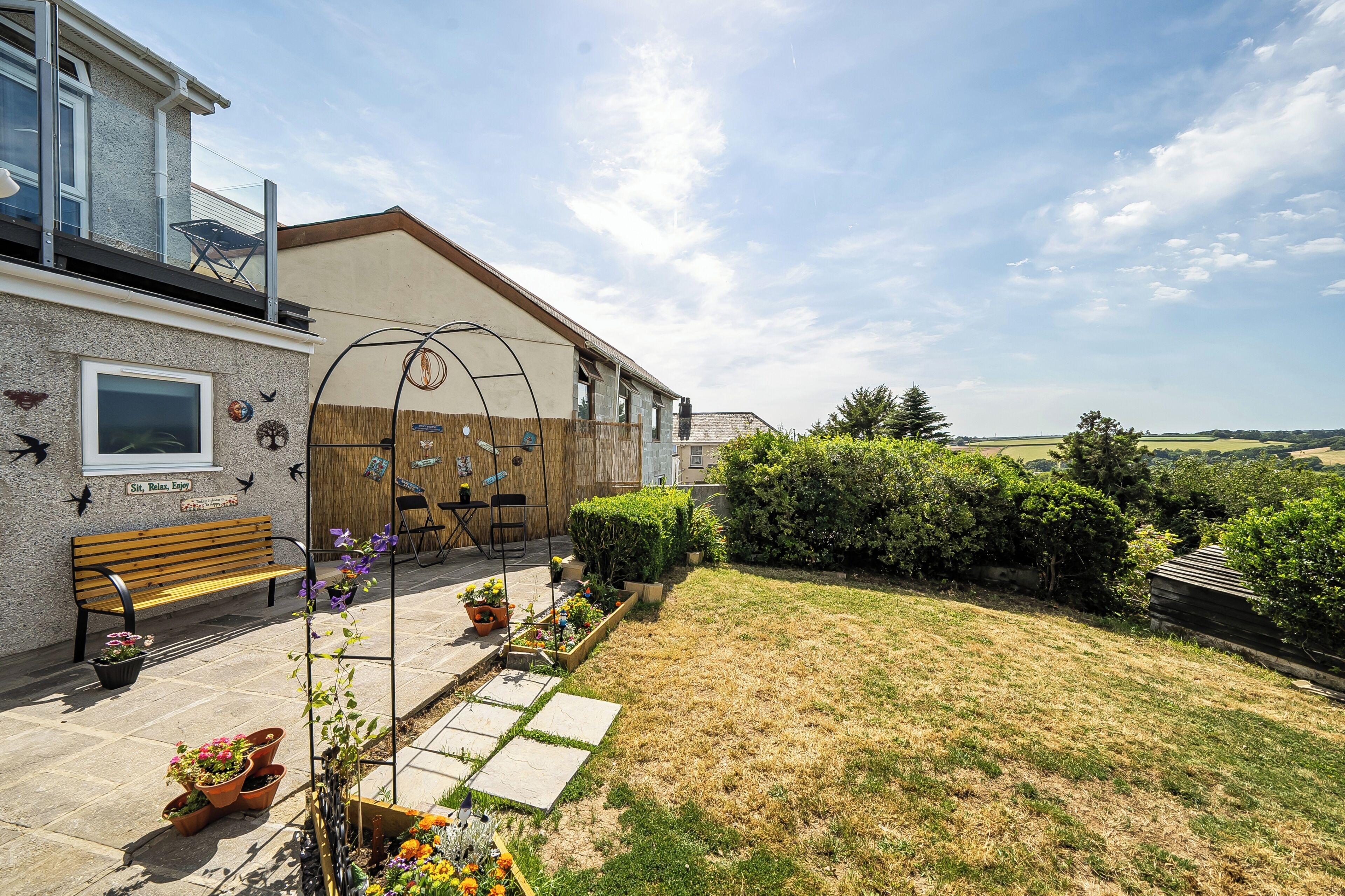 A residential property with a patio, outdoor seating, a wooden bench, and a view of the countryside.