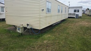 En etplans campingvogn med fladt tag, en lille veranda og et udvendigt skab på siden.