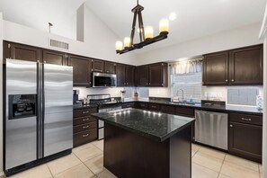 A modern kitchen with dark wood cabinets, stainless steel appliances, a granite countertop island, and a pendant light fixture. - Foothills Golf Escape - Phoenix Pool House backing up to Foothills Golf Club (Phoenix)
