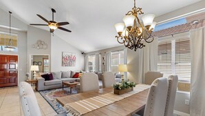 Ein geräumiges Wohnzimmer mit Esstisch, Stühlen, Deckenventilator und einer Chandelüster.