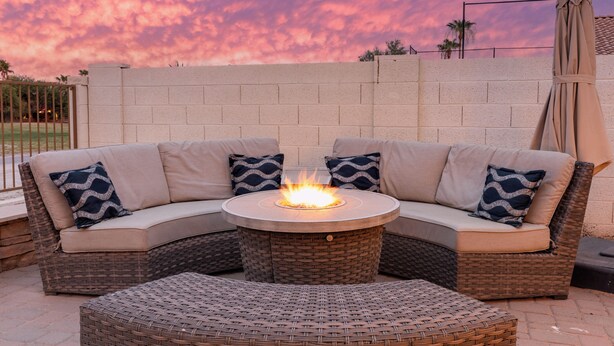 Ein Ecksofa mit rundem Tisch und Kamin, vor einer Ziegelwand mit Sonnenuntergangshimmel.