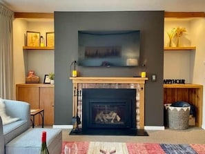Ein Wohnzimmer mit Kamin, einem flachbildfernseher darüber, einer Couch und einem Couchtisch.