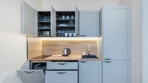 A compact kitchenette with open cabinets, a wooden countertop, and a built-in dishwasher. - Nawrot Downtown Chic Studio #A (Łódź)