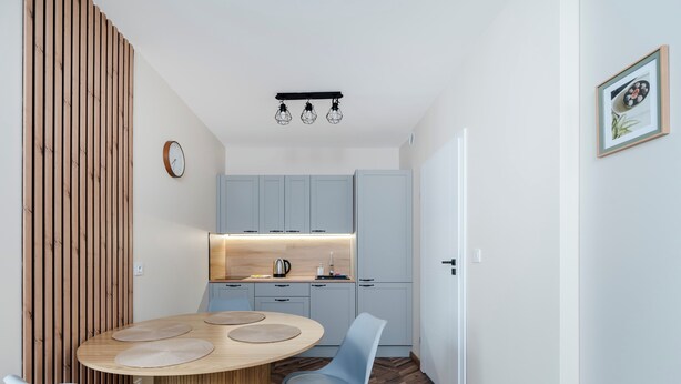 A modern kitchen with light blue cabinets, a wooden dining table with two chairs, and a hanging light fixture. - Nawrot Downtown Chic Studio #A (Łódź)