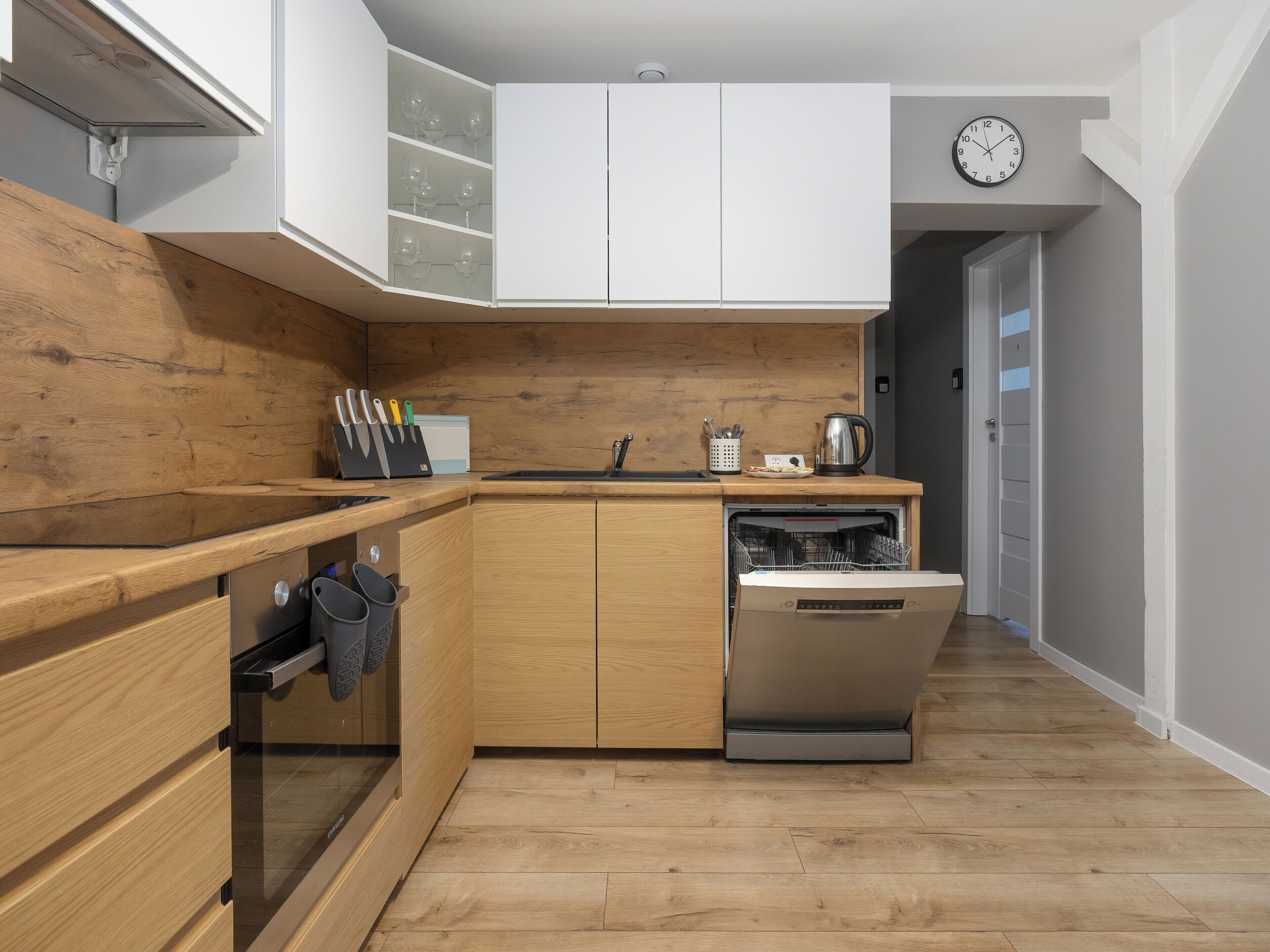 Une cuisine moderne avec des meubles en bois, un lave-vaisselle encastré et une horloge au mur.