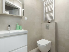Un baño con un lavabo blanco, artículos de aseo verde, un inodoro y un perchero para toallas.