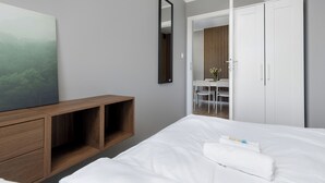 A modern hotel room with a bed, a wooden bedside table, a desk with chairs, and a wardrobe. - Jagiellońska Central Guest Spot #2 (Szczecin)