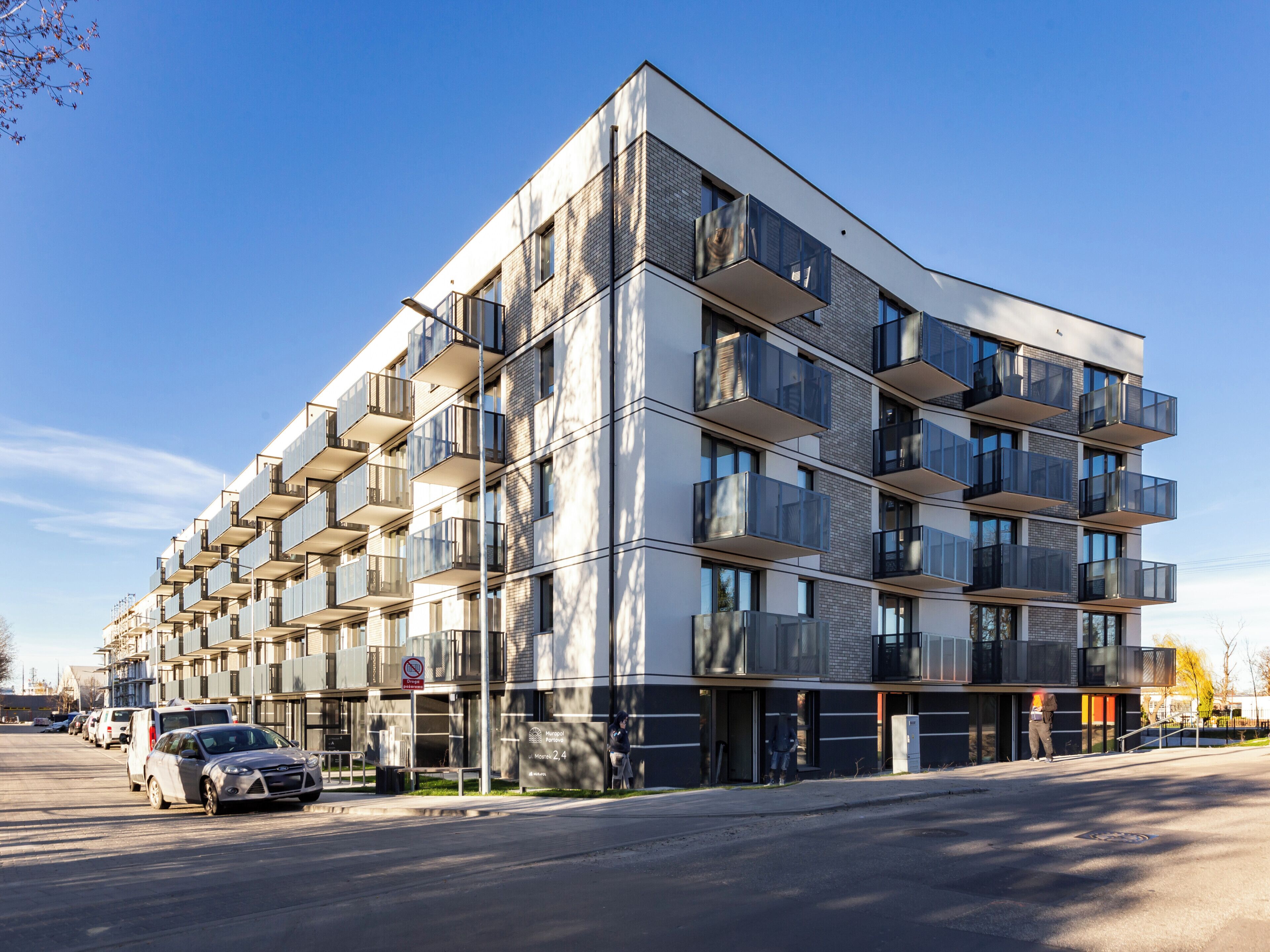 Een modern meerlaags gebouw met balkons, een parkeerplaats en een bord dat een ziekenhuis aanduidt.