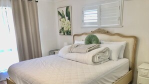Una cama bien hecha con un edredón blanco acolchado, una almohada verde y toallas blancas dobladas.