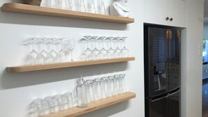 Tres repisas de madera con cristalería transparente y un refrigerador negro.