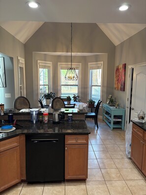 A kitchen with a central island, a dining area with a table and chairs, and a view of the outdoors through windows.
