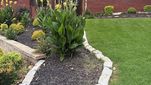 A residential house with a brick facade, a well-maintained lawn, and a flower bed with yellow flowers. - Main level access = 2 BR, 2 private baths, and much more. Wheelchair accessible. (Braselton)