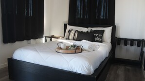 A neatly made bed with a tray of toiletries, a bedside table, and a headboard with a black curtain.