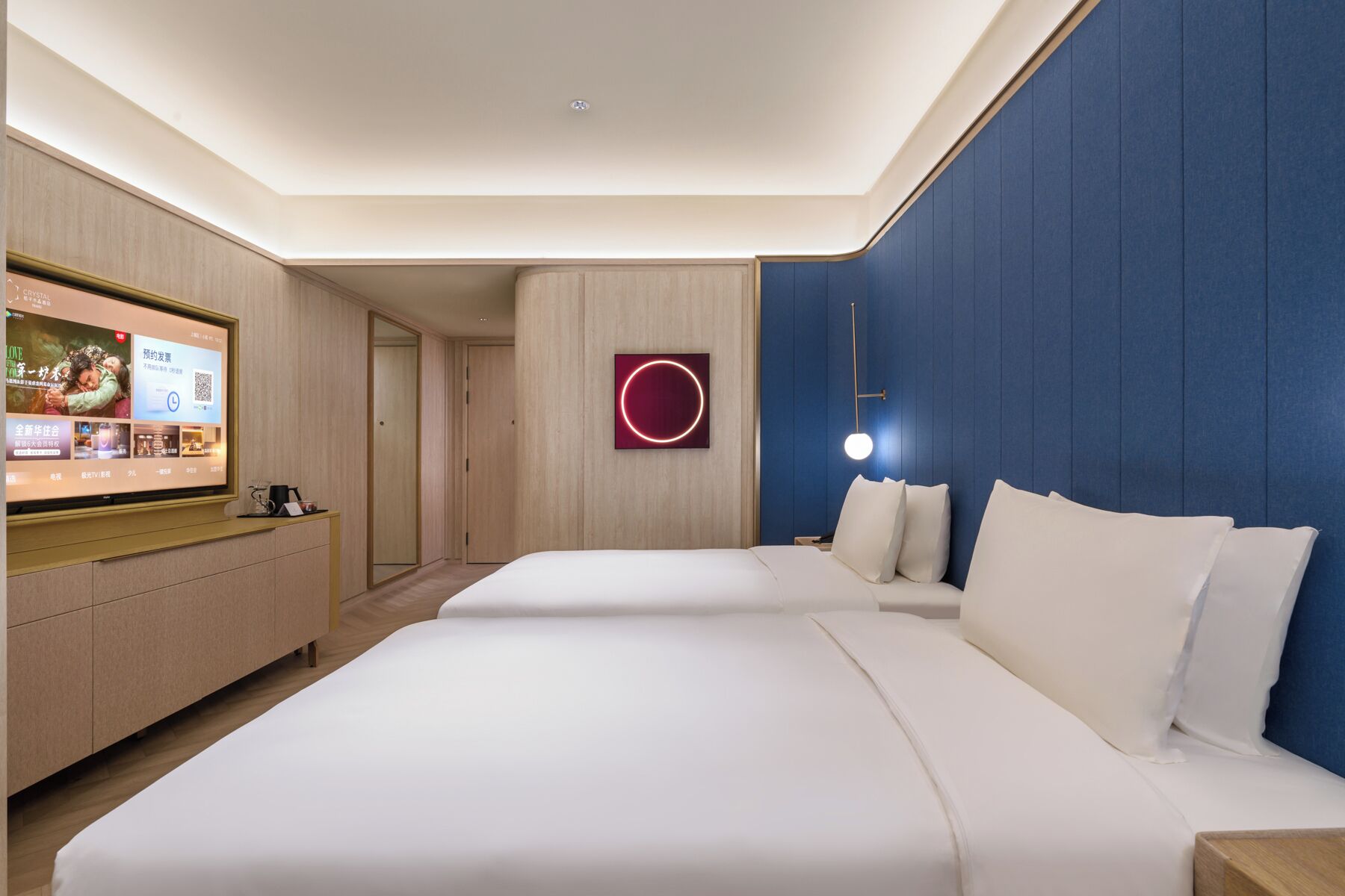 Habitación de hotel con una cama grande, un escritorio con televisión de pantalla plana y una lámpara circular fijada a la pared.