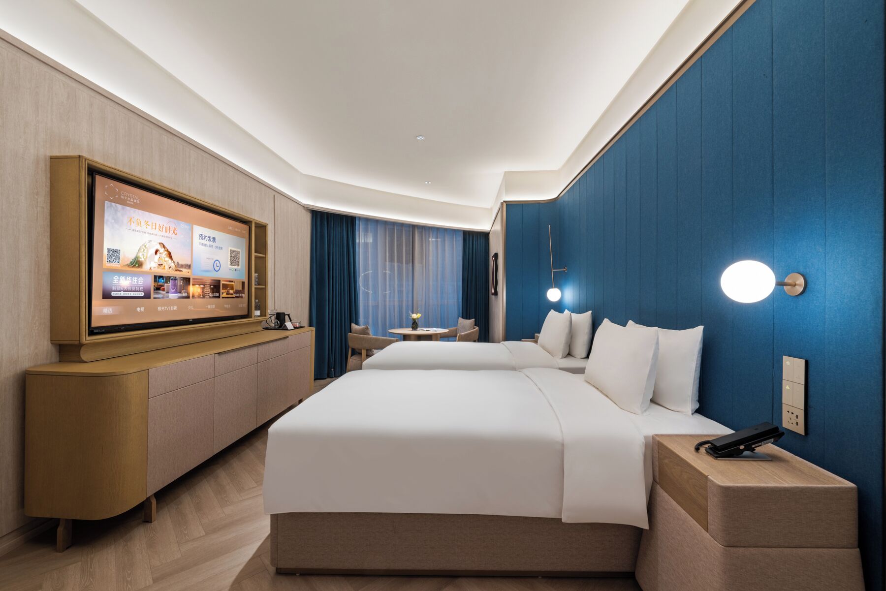 A hotel room with a large bed, a desk, a chair, a TV mounted on the wall, and a blue accent wall.
