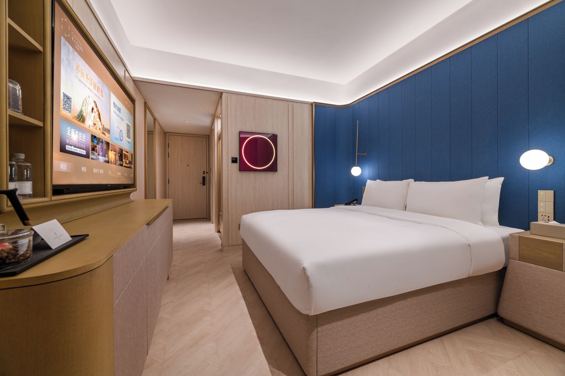 A hotel room with a bed, bedside table, and a desk with a computer and a phone.