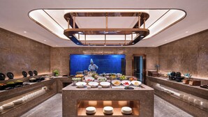 Eine moderne Hotellobby mit einem zentralen Buffetbereich, einer blauen Akzentwand und einem Koch, der Essen zubereitet.