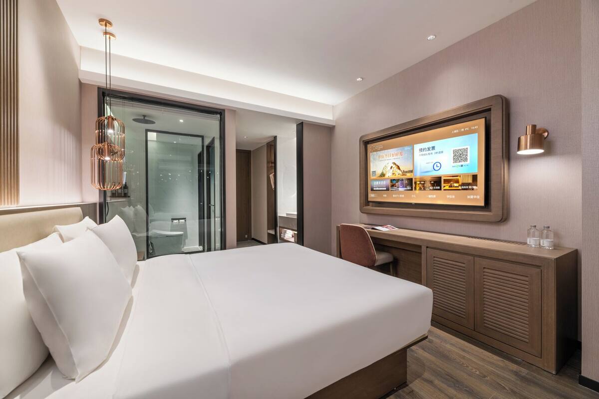 A hotel room with a bed, a desk, a television, and a glass shower enclosure.