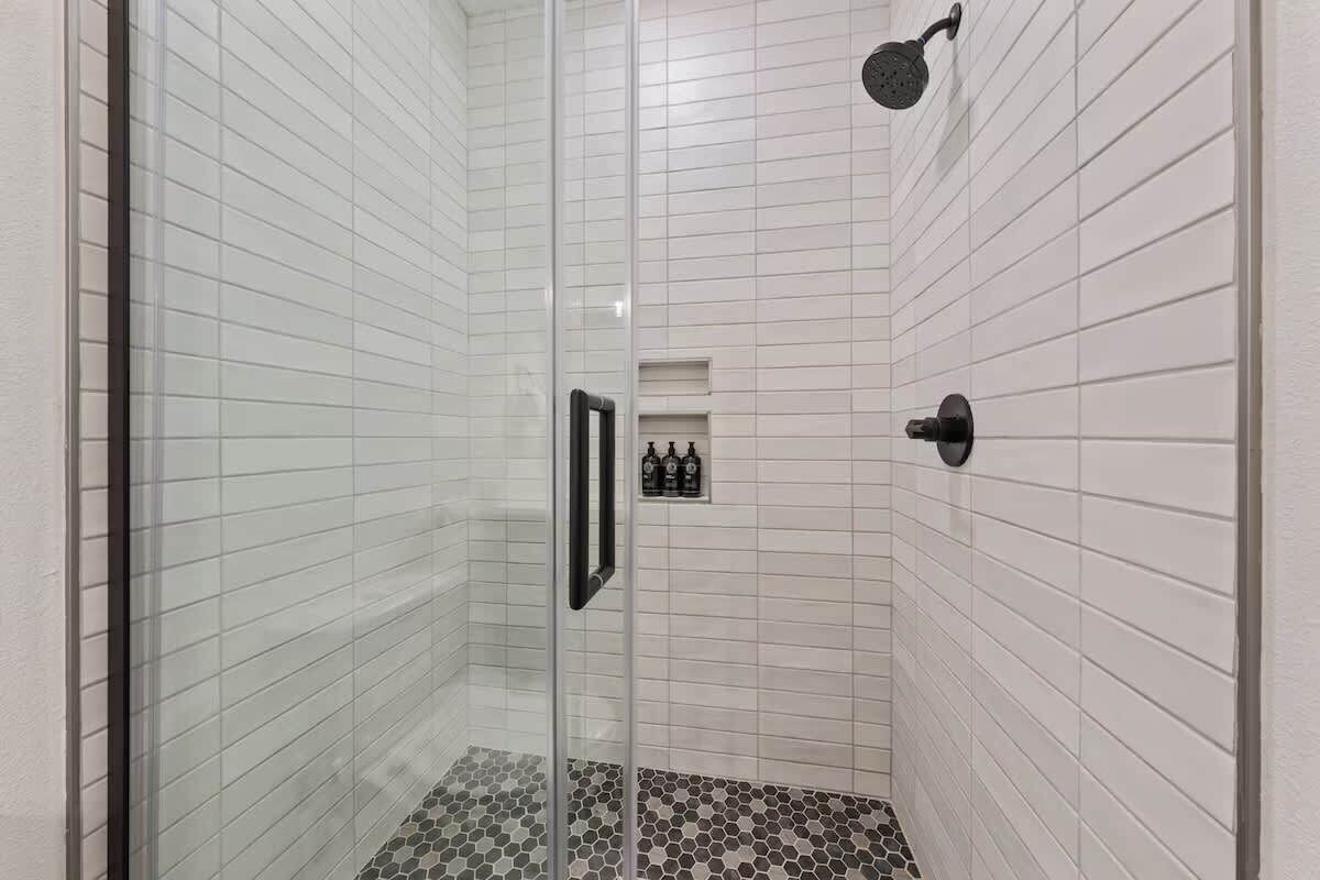 A glass-enclosed shower with white tiled walls and a hexagonal tile floor.