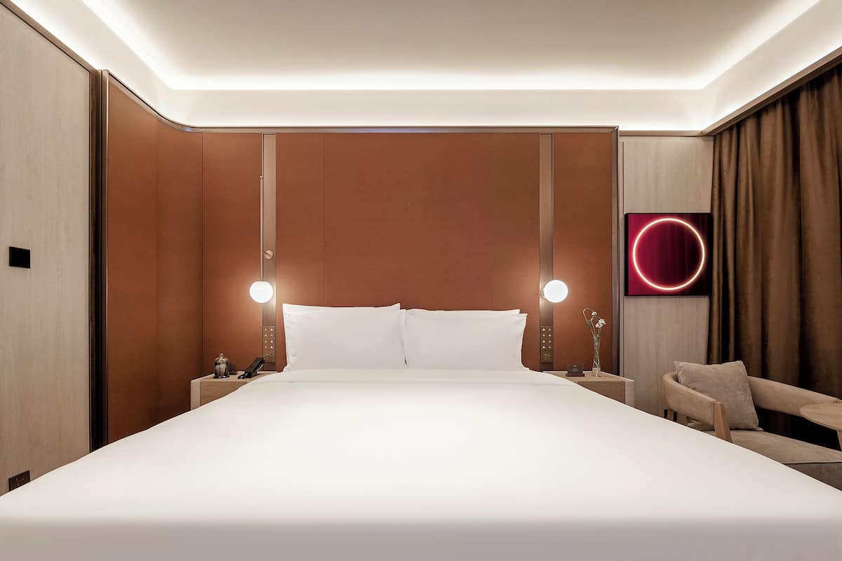 Et moderne hotelværelse med en stor seng, sengeborde med lamper, et fladskærms-tv og et siddeområde.
