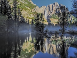Un lago sereno con reflejos de árboles y montañas, rodeado por un bosque.