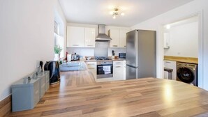 A modern kitchen with white cabinets, stainless steel appliances, and a wooden floor. - Entire 5 Bed home in Bristol United Kingdom (Pucklechurch)