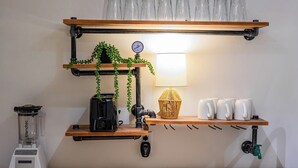 Ett kök med en kaffemaskin, en mixer, en tryckkokare och en hylla med koppar och en lampa.