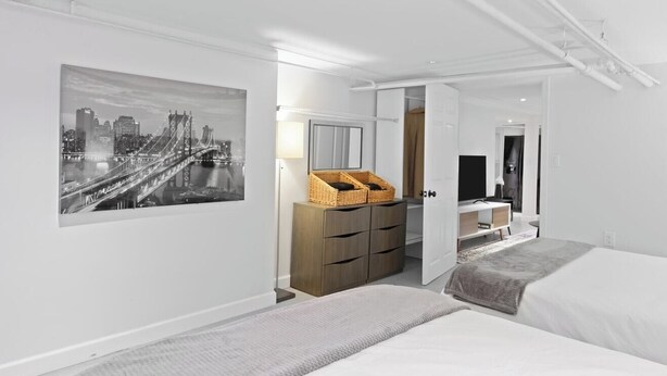 Ett modernt hotellrum med en säng, en byrå, en spegel och en tavla med en stadsbild på väggen.