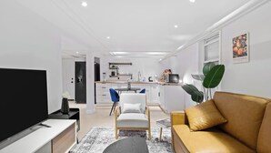 Ett modernt vardagsrum med en platt-TV, en soffa, ett soffbord och en matplats med en stol och ett bord.