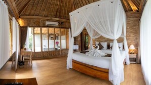 A room with a canopy bed, a wooden floor, and a view through a glass door.