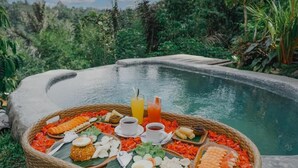 A dining setup with a variety of food items and drinks by a poolside, surrounded by lush greenery.