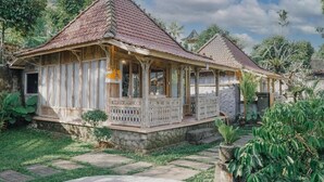 A traditional wooden house with a tiled roof, a porch with a railing, and a stone pathway leading to the entrance.