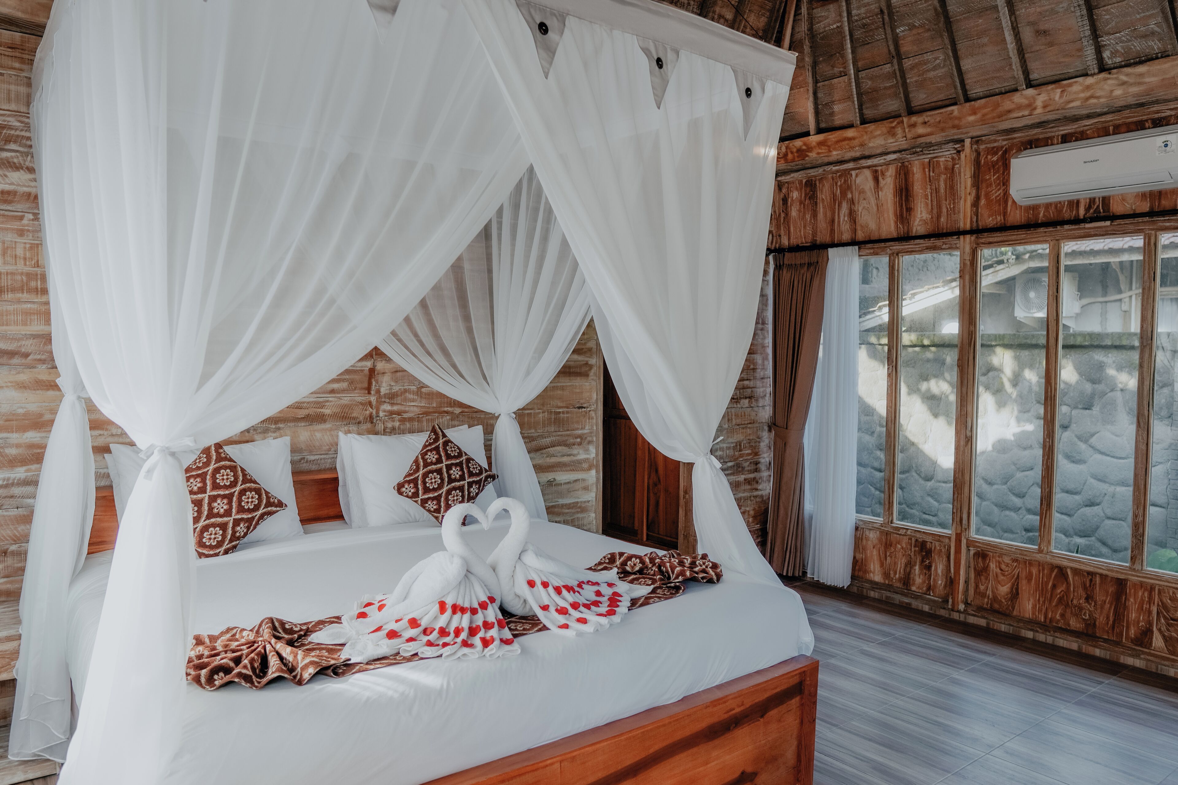 A bed with a canopy, patterned pillows, and a towel arrangement.