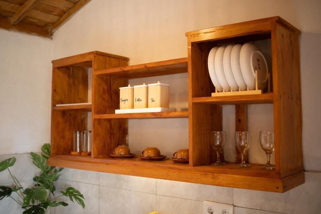 Ein Holzregal mit beschrifteten Behältern für Zucker, Kaffee und Tee, sowie ein Tellerhalter mit Tellern und Gläsern.
