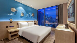A modern hotel room with a large bed, a desk, and a city view.