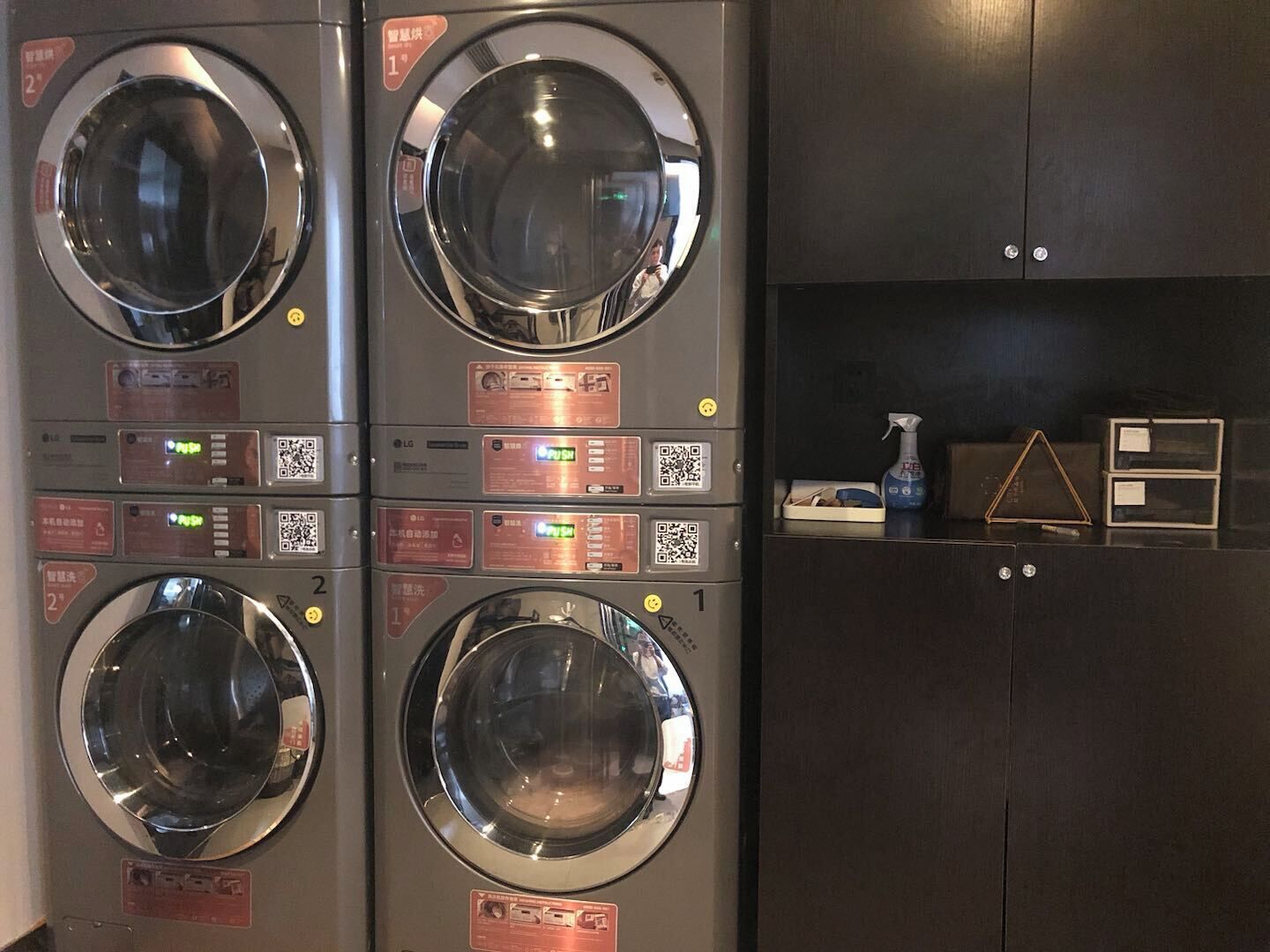 A laundry facility with four washing machines, each with a digital display and QR code.