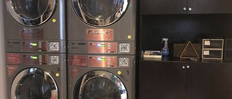A laundry facility with four washing machines, each with a digital display and QR code.