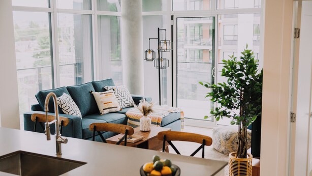 A modern kitchen with a sink, dining table, and chairs, a blue sofa with patterned cushions, and a potted plant. - Beachside Luxury Suite | Pool, hottub, Sleeps 6 (Kelowna)