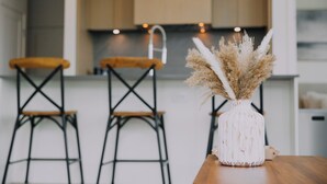 A modern kitchen with wooden chairs, a white vase with dried flowers, and a wooden table. - Beachside Luxury Suite | Pool, hottub, Sleeps 6 (Kelowna)