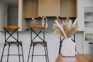 A modern kitchen with wooden chairs, a white vase with dried flowers, and a wooden table. - Beachside Luxury Suite | Pool, hottub, Sleeps 6 (Kelowna)