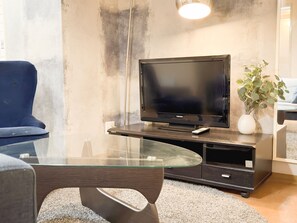 Un salon moderne avec un téléviseur à écran plat posé sur un meuble en bois, une table basse en verre, un fauteuil bleu et une plante en pot.