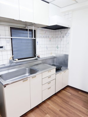 Eine Küche mit Spüle aus Edelstahl, einem Fenster mit Metallgitter und einer gefliesten Spritzschutzleiste mit floralen Mustern.