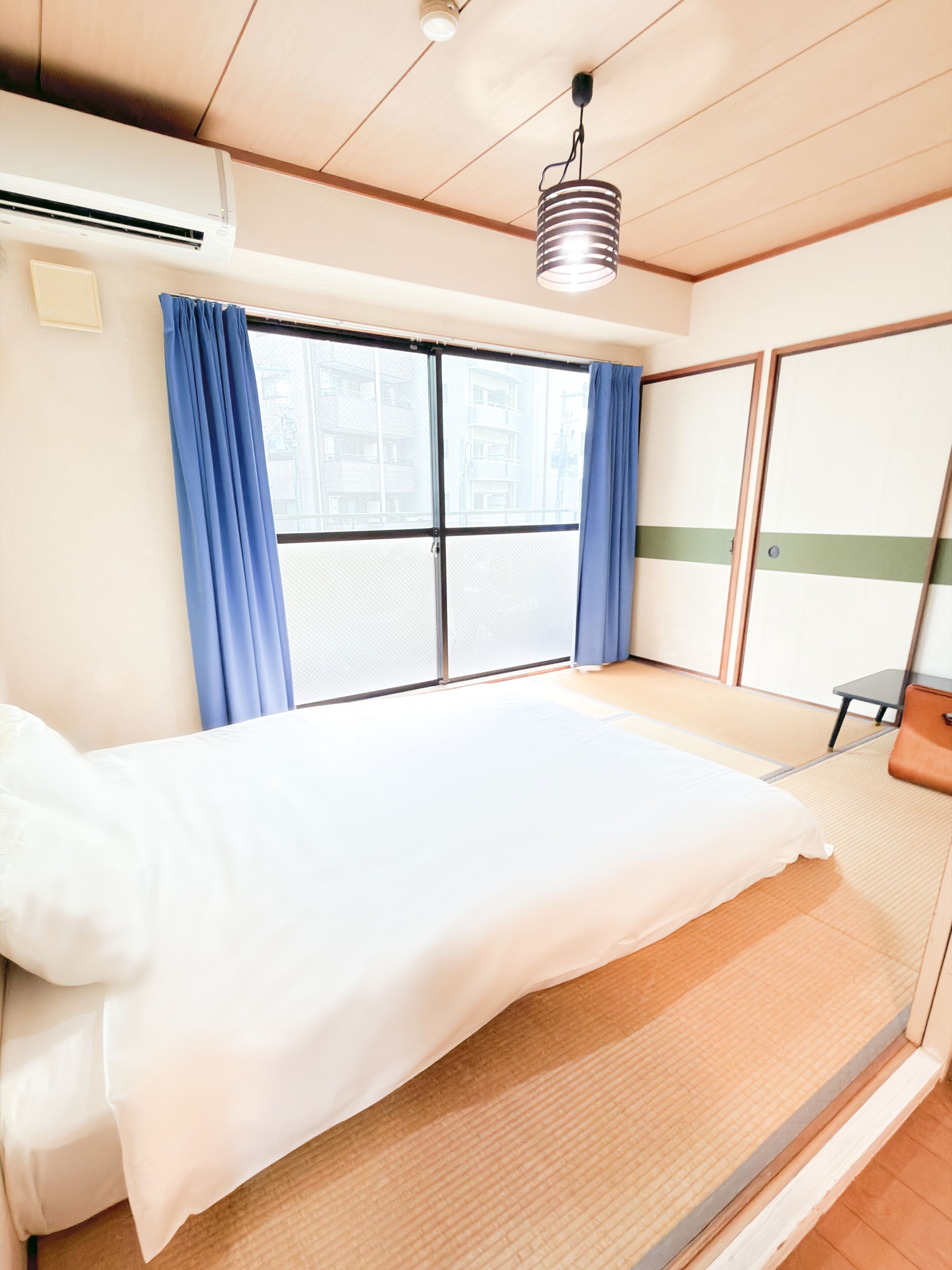 Habitación de hotel con cama, ventana con cortinas, ventilador de techo y vistas a edificios.