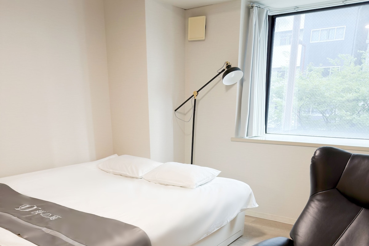 Ein Schlafzimmer mit einem Bett, einem Sessel, einer Lampe und einem Fenster.