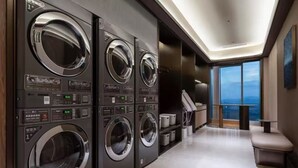 A modern laundry room with multiple washing machines, a bench, and a view of the city. - Orange Crystal Hangzhou Tonglu Station (Hangzhou)